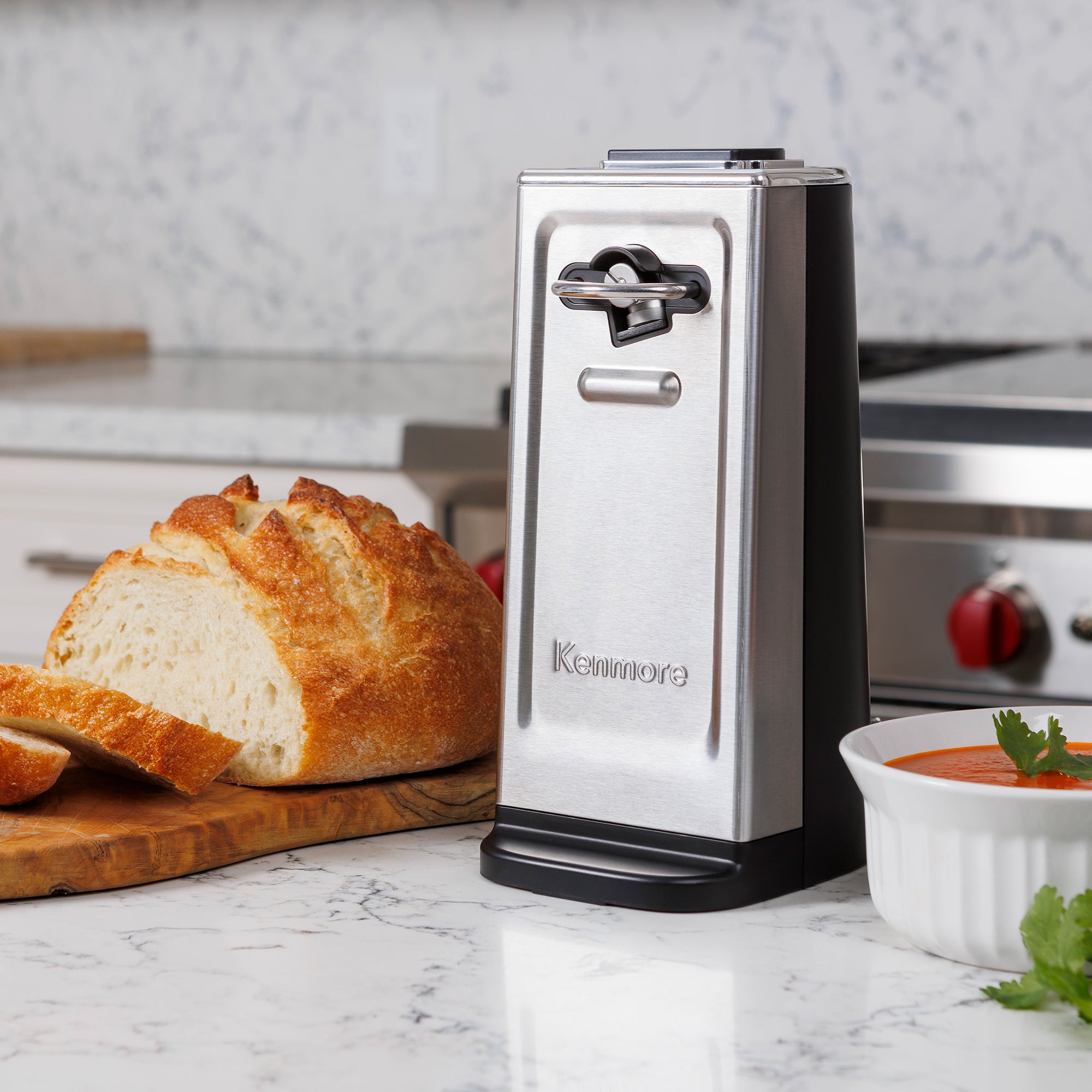 Kenmore stainless steel smooth-edge can opener on a white marble countertop with a loaf of bread beside it
