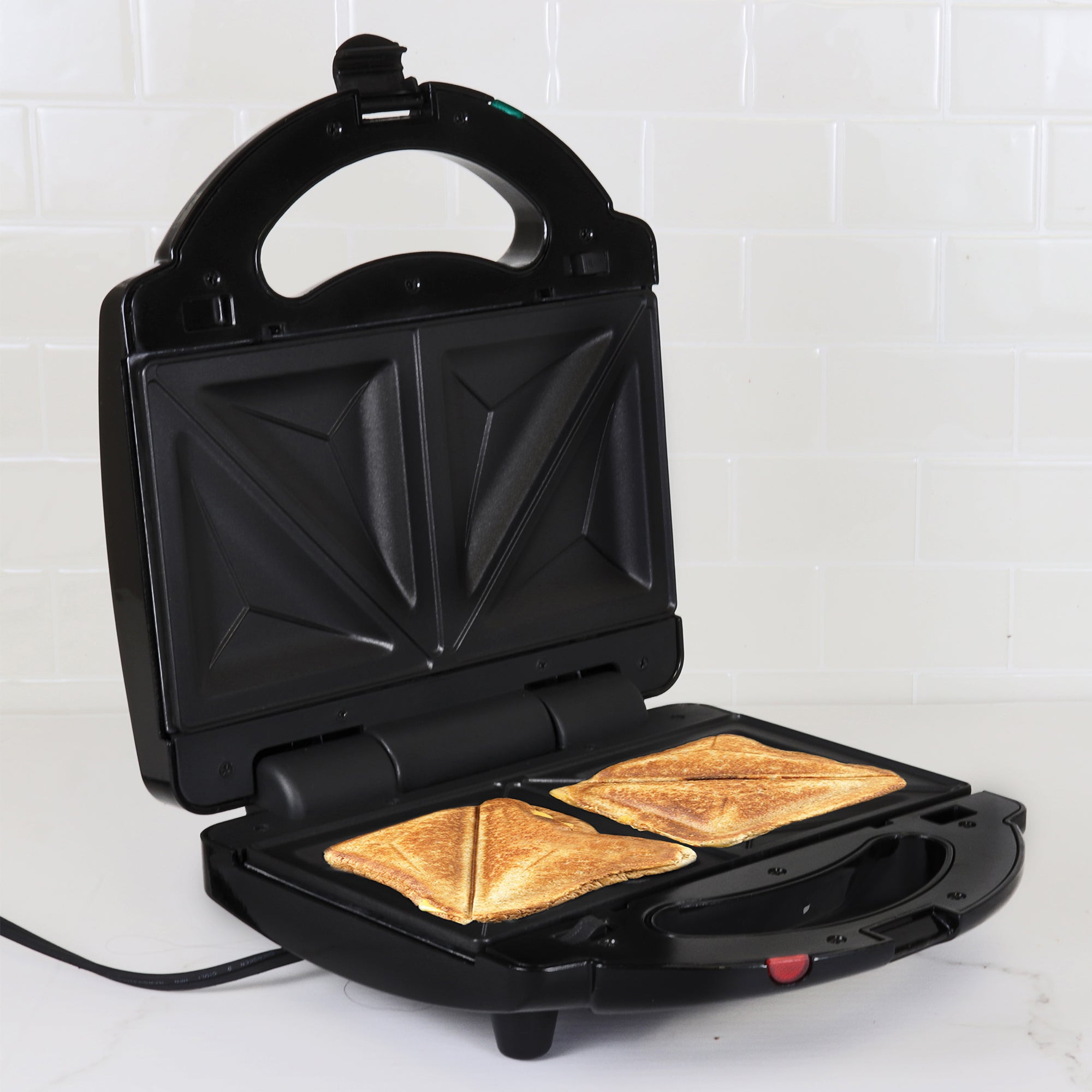 Lifestyle image of 4 in 1 grill open with grilled cheese sandwiches inside on a white countertop with a white tile backsplash behind