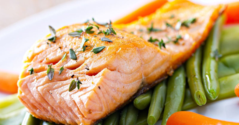 Closeup photo of a cooked salmon filet with herbs sprinkled on top on a bed of cooked vegetables