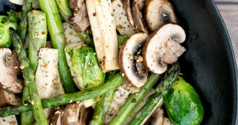Closeup image of cooked vegetables including mushrooms, asparagus, and brussel sprouts