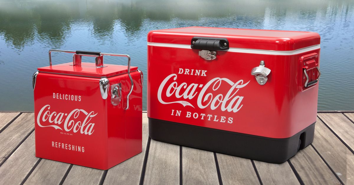 Two red cooler ice chests, one more square and one rectangular sit on a wooden deck. In the background is a blue lake and reflected in the lake are green trees.