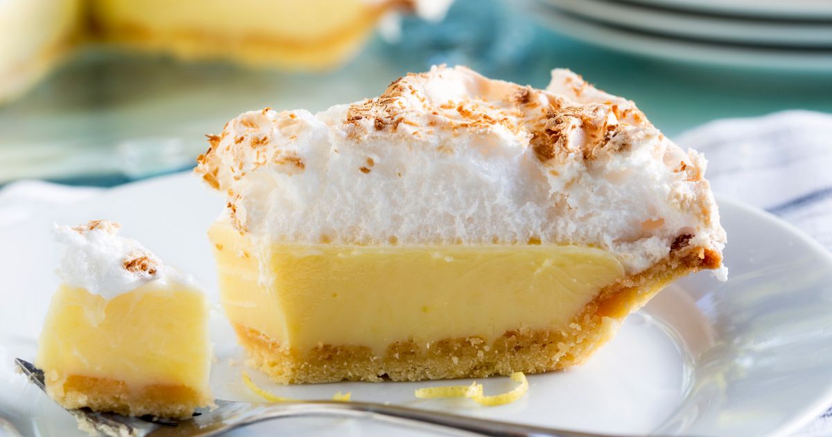 Picture of a slice of lemon meringue pie on a white plate with a fork