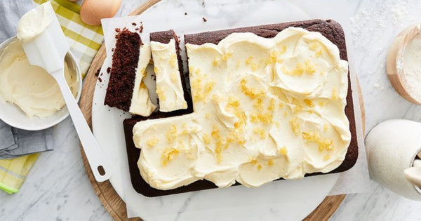 Photo of a dark colored spiced teacake with white frosting with light yellow pieces of ginger sprinkled over top