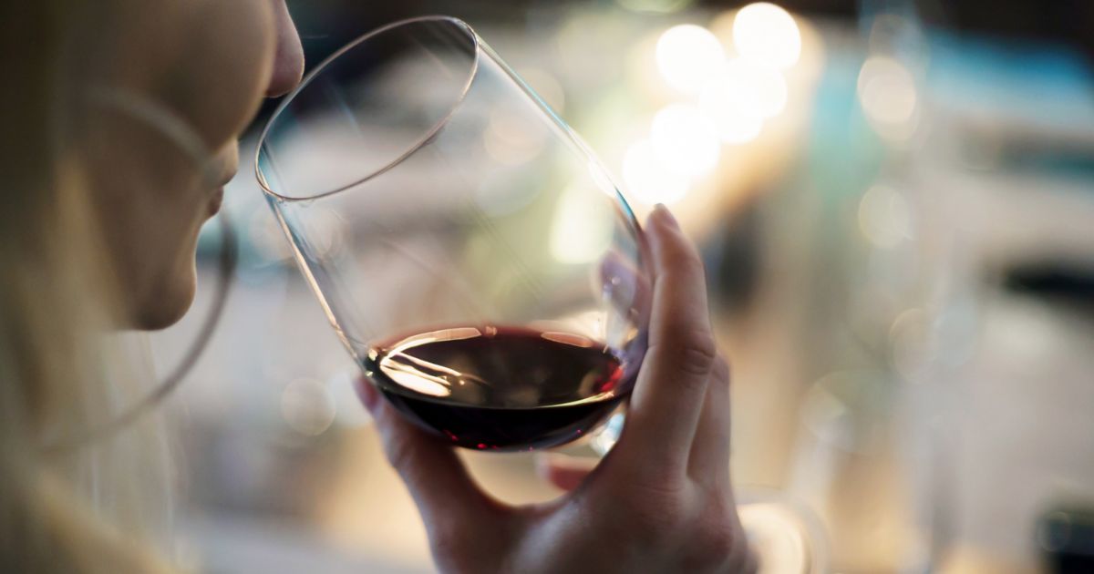 Closeup image of a person with light skin and long blonde hair sipping from a glass of red wine