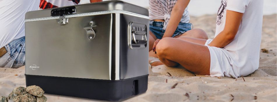 Lifestyle image of people sitting on a sandy beach with a stainless steel 51L ice chest in the foreground