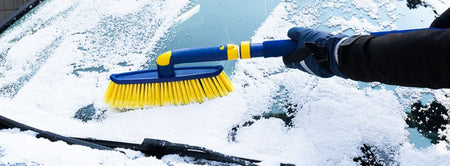 Closeup image of a yellow and blue snow brush being used to clear snow off a car windshield