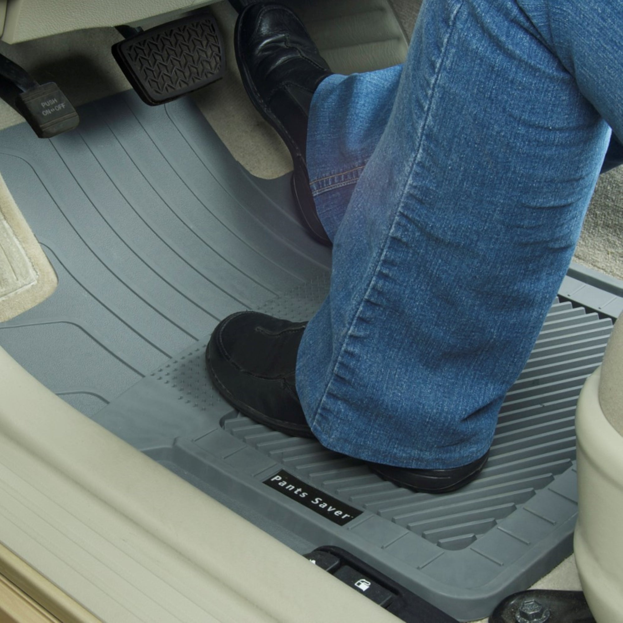 Lifestyle image of a gray PantsSaver custom fit car mat installed in the driver's seat of a vehicle with a person wearing blue jeans and black shoes sitting in the driver's seat