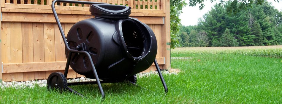 Lifestyle image of wheeled tumbling composter set up on grass in front of a wooden fence