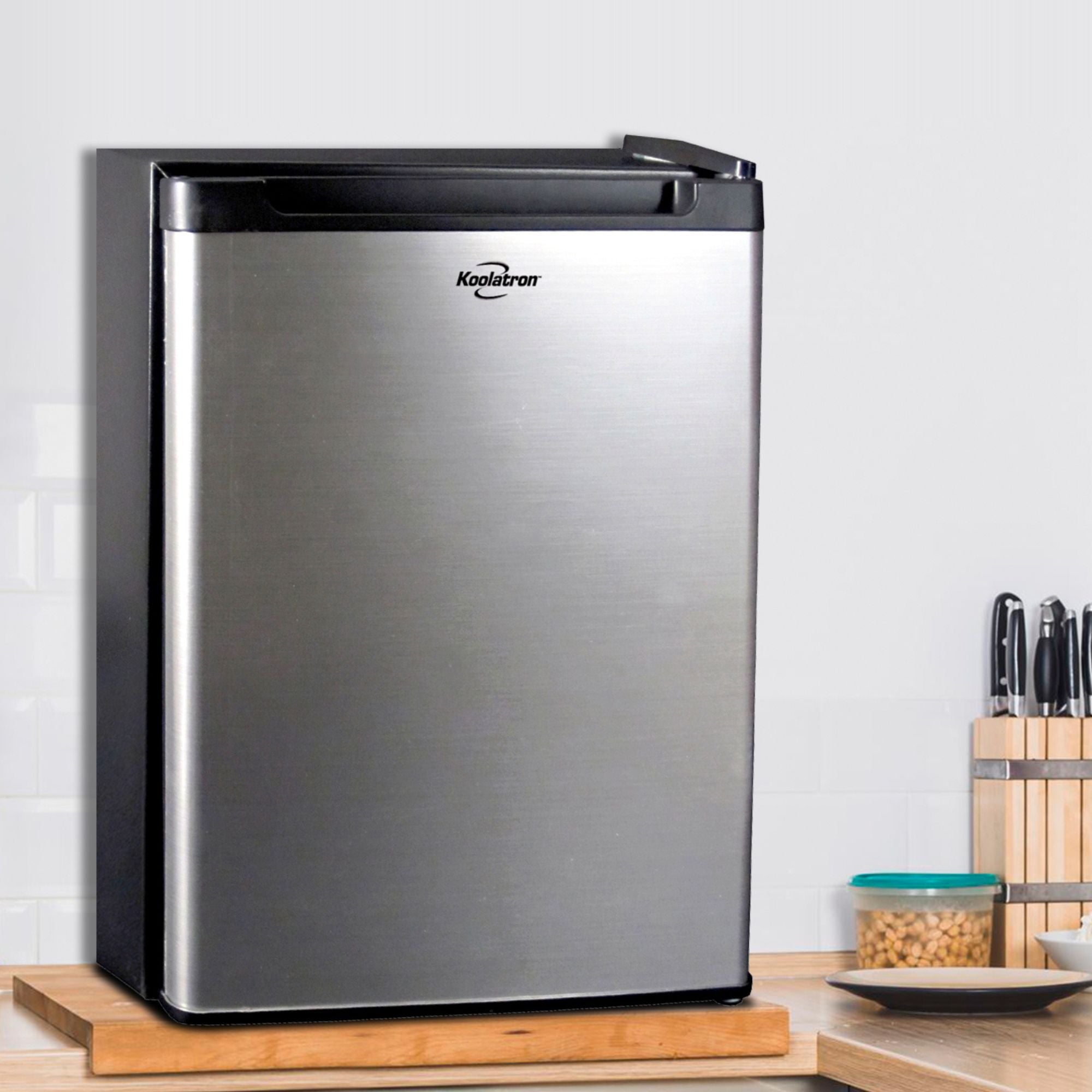 Black and stainless steel compact fridge on a light colored wooden countertop with a white tile wall behind
