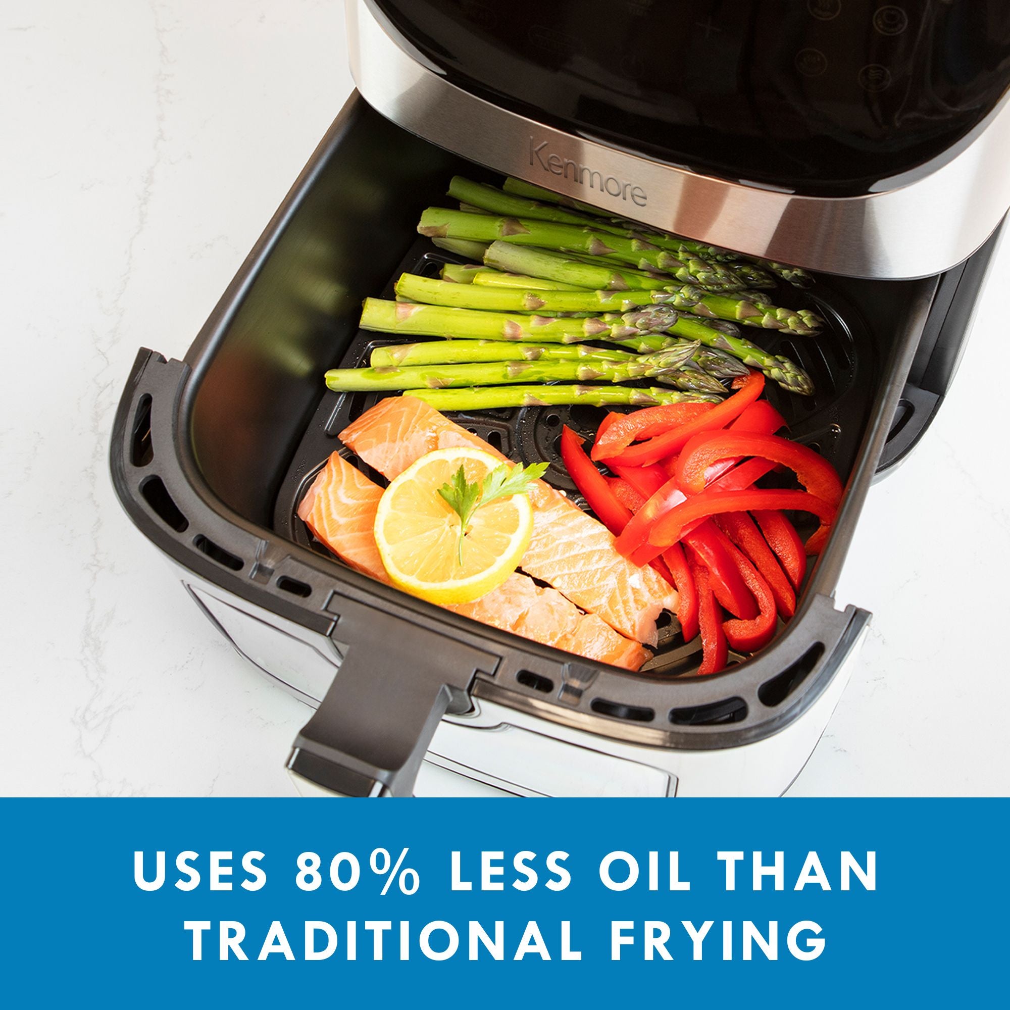 Closeup of air fryer basket containing a piece of salmon topped with a lemon slice, a bunch of asparagus spears, and sliced red peppers. Text below reads, "Uses 80% less oil than traditional frying."