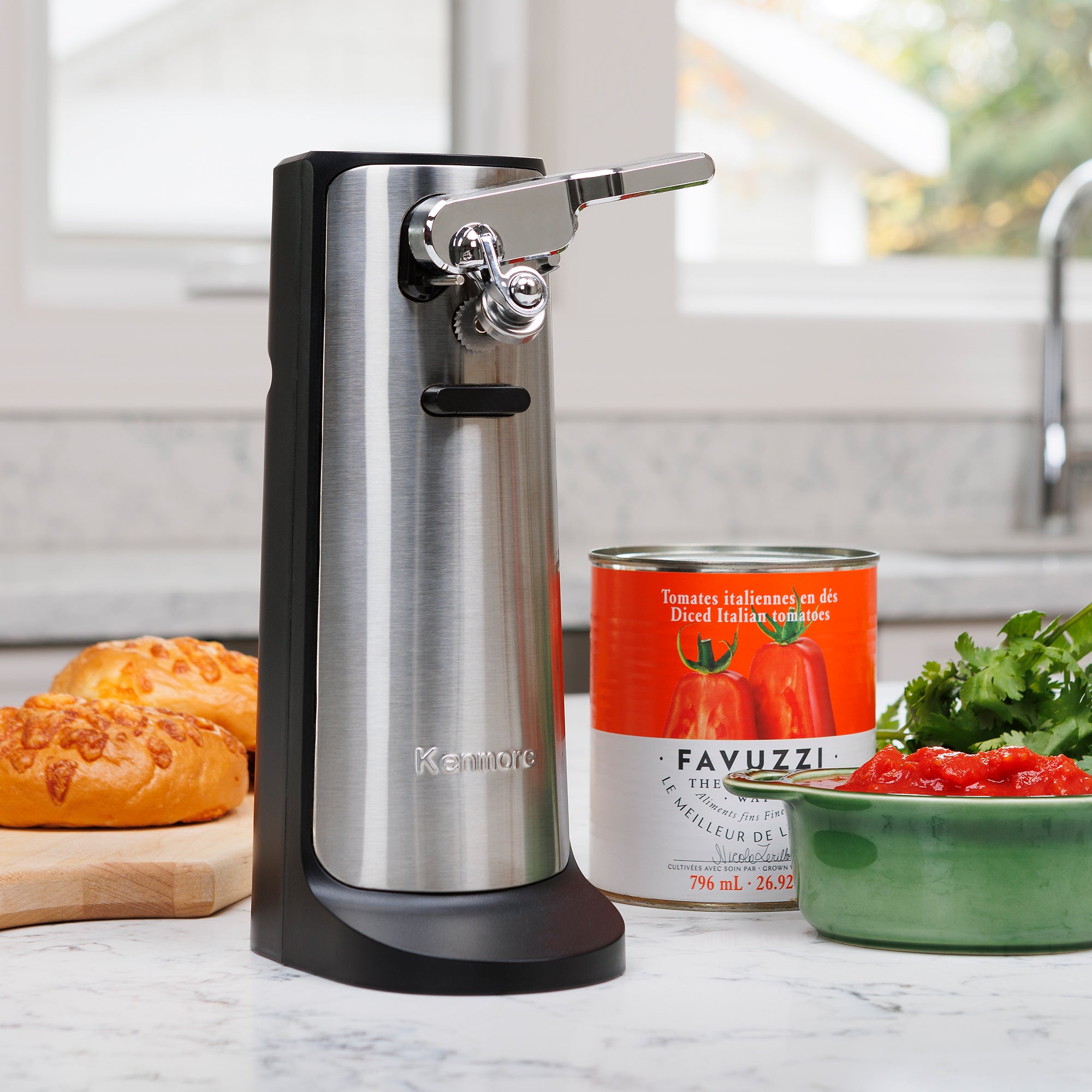 Kenmore multifunction electric can opener with knife sharpener and bottle opener surrounded by food on a white marble countertop