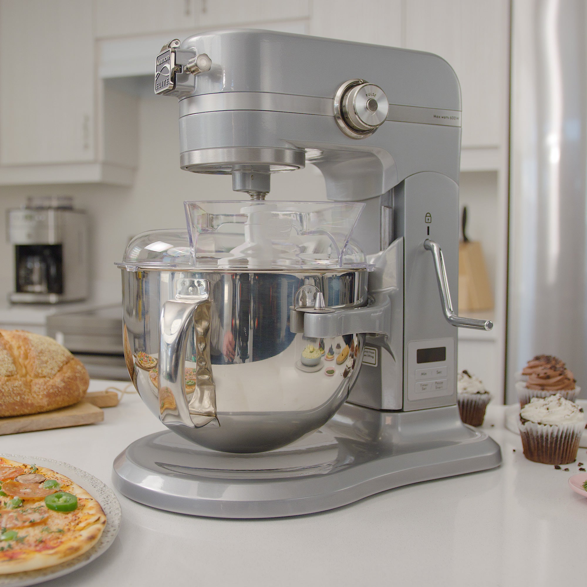 Kenmore bowl-lift stand mixer on a white kitchen counter with a loaf of bread, pizza, and cupcakes arranged around it