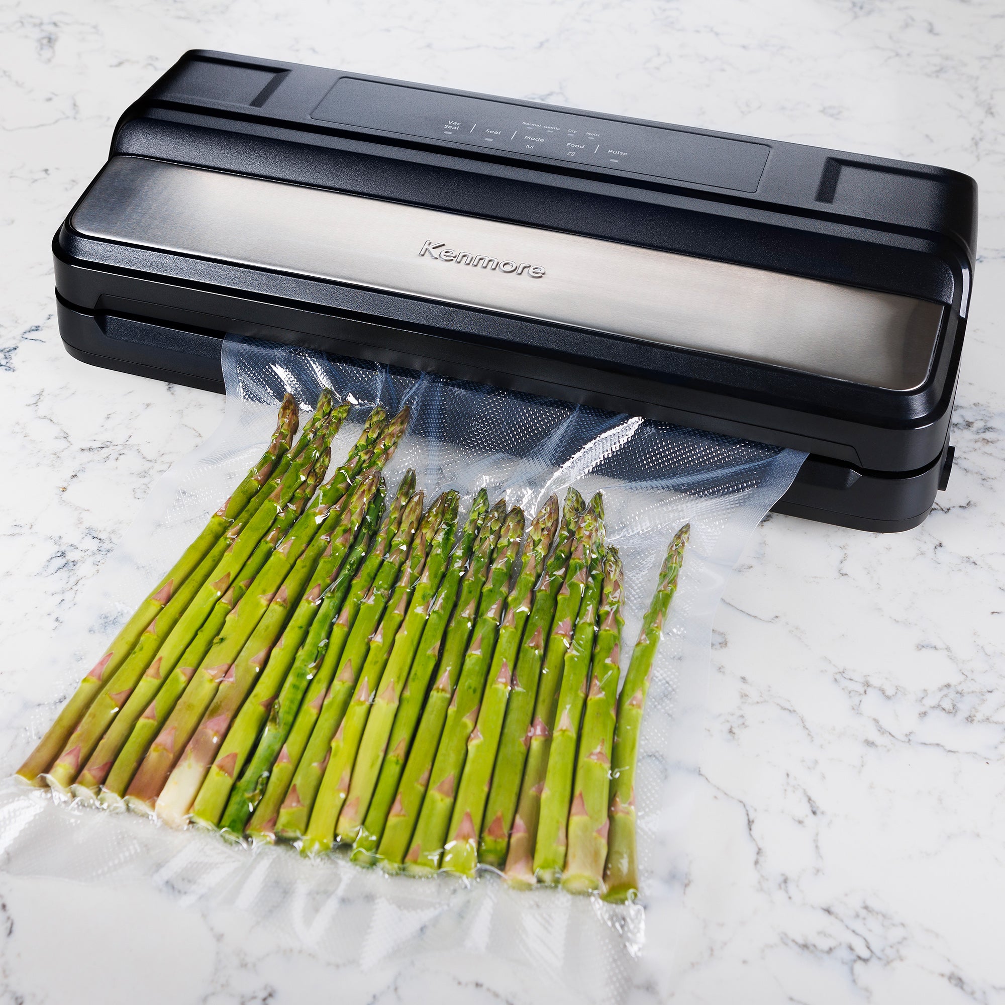 Kenmore vacuum food sealer sealing a bag of asparagus on a white and gray marble surface