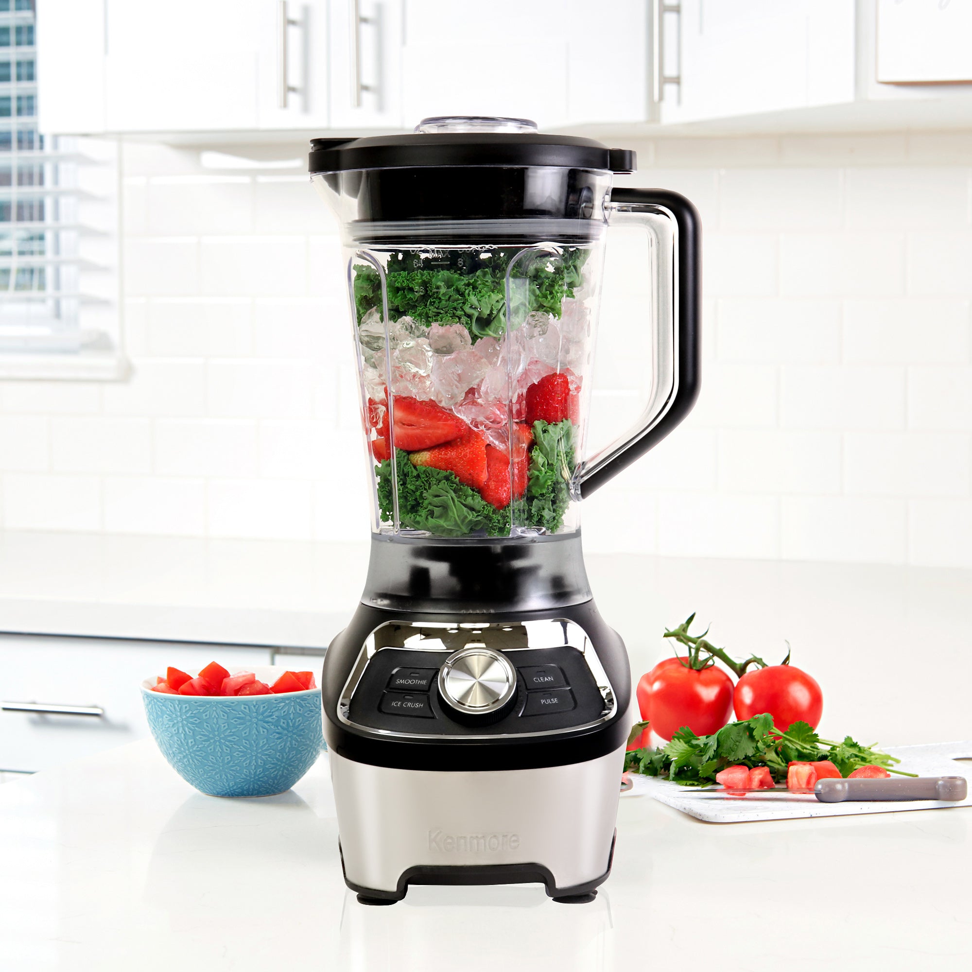 8 cup stand blender filled with salsa ingredients on a white countertop with chopped vegetables arranged around it.