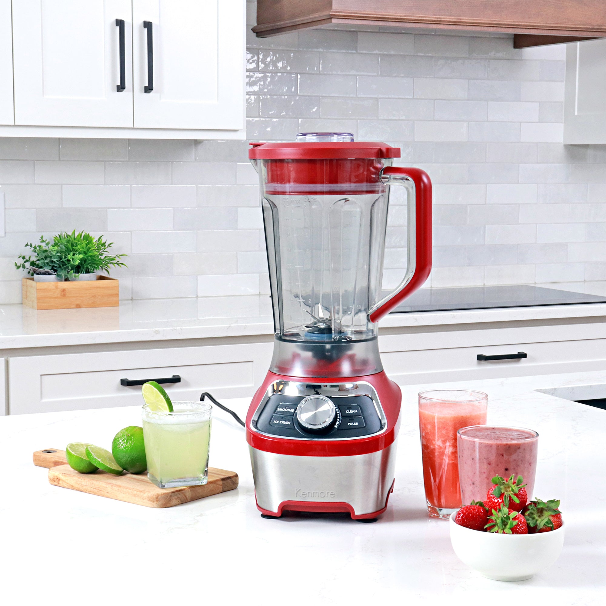 64 oz stand blender on a white countertop with glasses of juice, smoothie, and frozen lime margarita and a bowl of strawberries arranged around it. 