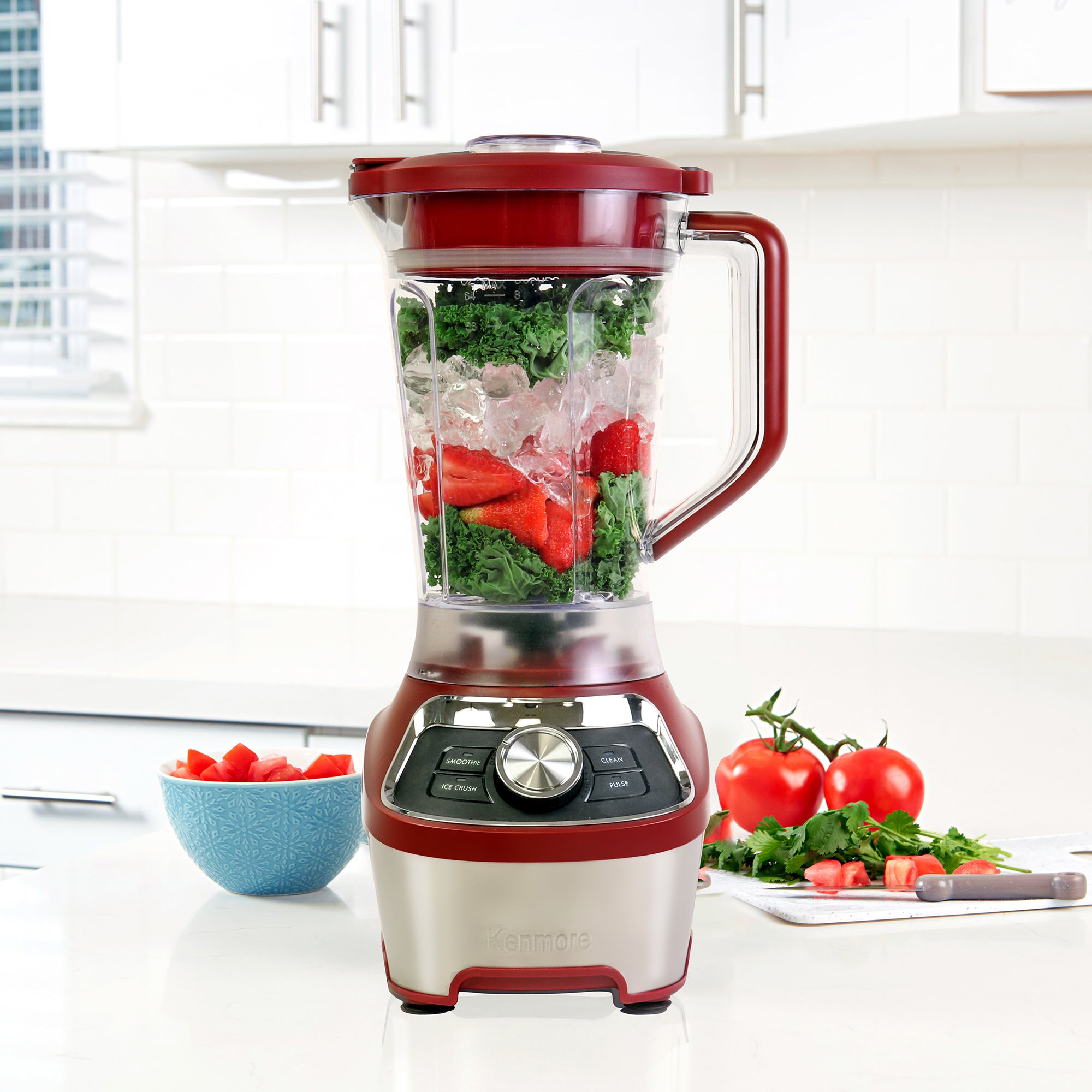 8 cup stand blender filled with salsa ingredients on a white countertop with chopped vegetables arranged around it.