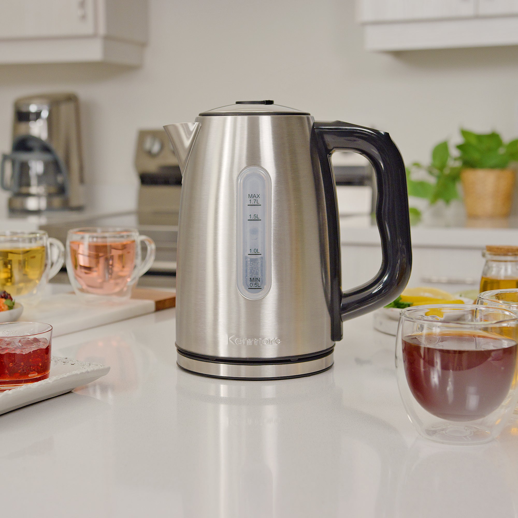 Kenmore stainless steel digital teakettle on a white marbled countertop surrounded by glass mugs of different types of tea
