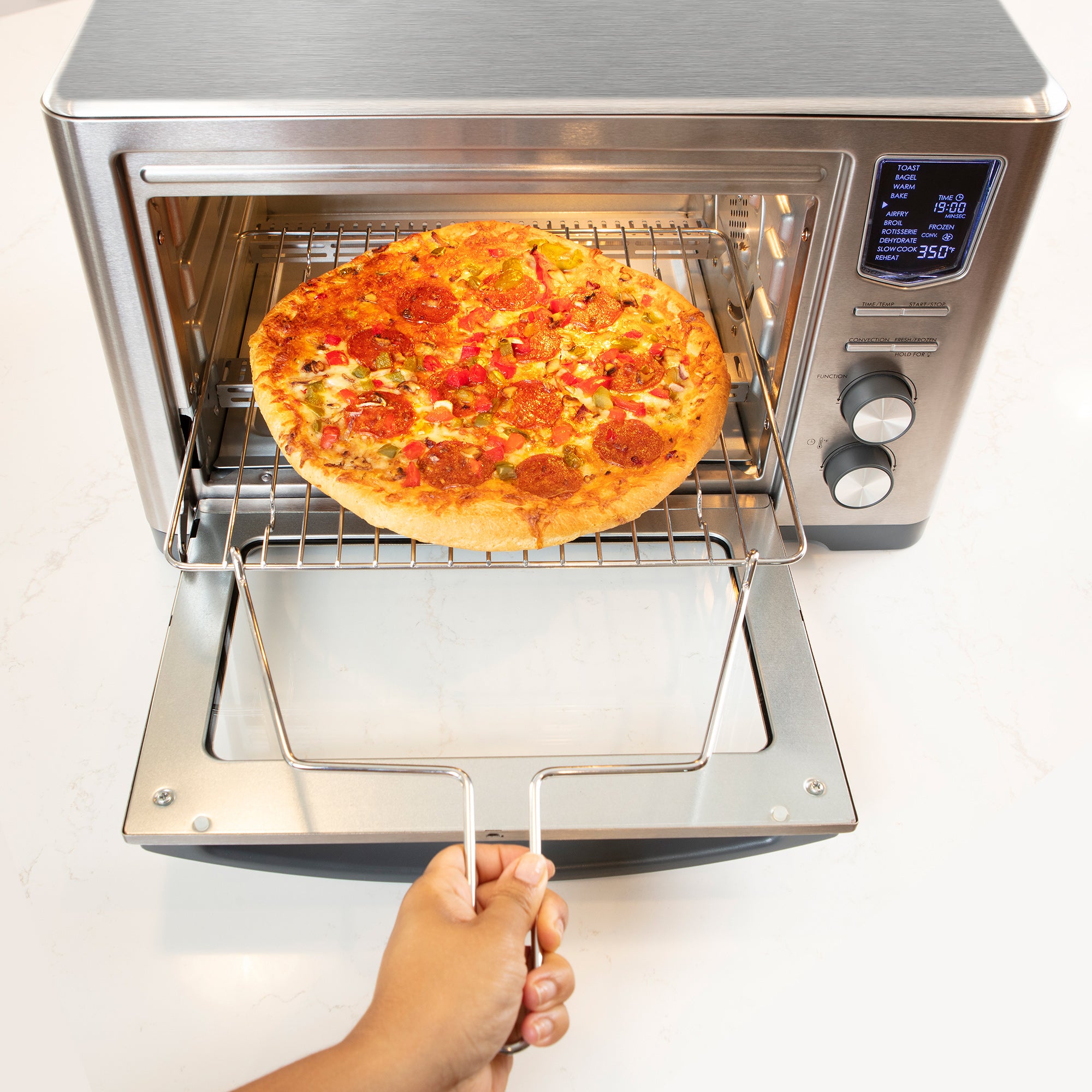 A person's hand using the rotisserie/rack handle to pull out the wire rack to check on a small pizza