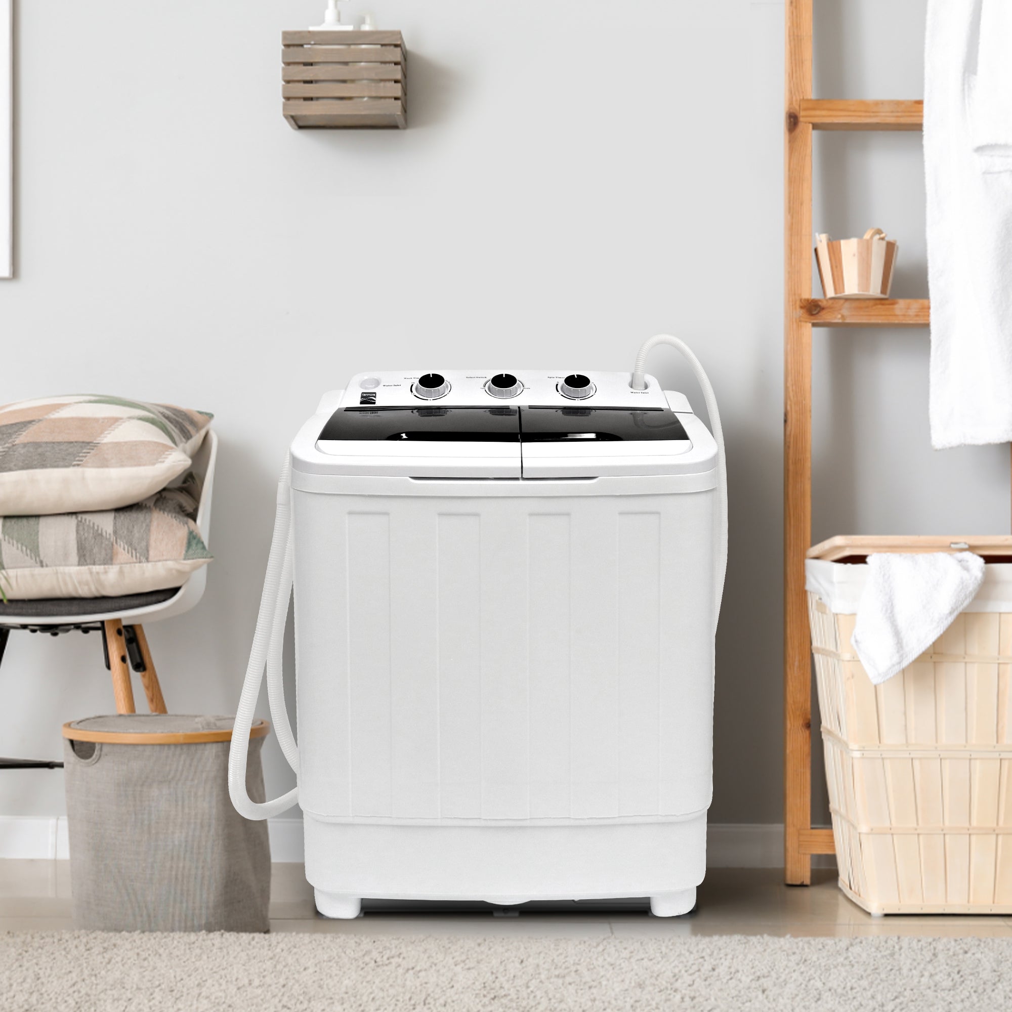 Kenmore twin tub washer and spinner on a beige carpet with a light gray wall behind and laundry hampers, a chair, and a wooden shelf on either side.