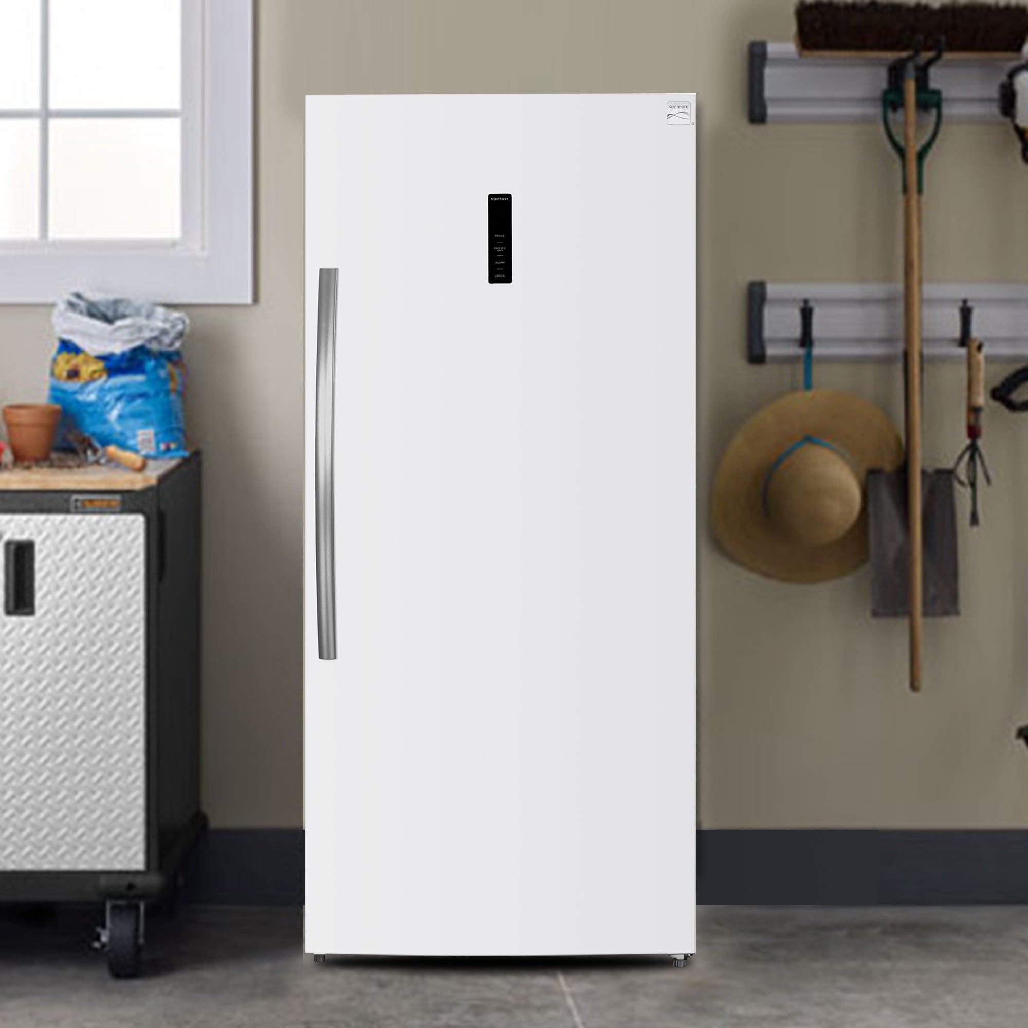 Kenmore convertible upright freezer/refrigerator, closed, in a workshop with garage with a tool bench and gardening tools beside it