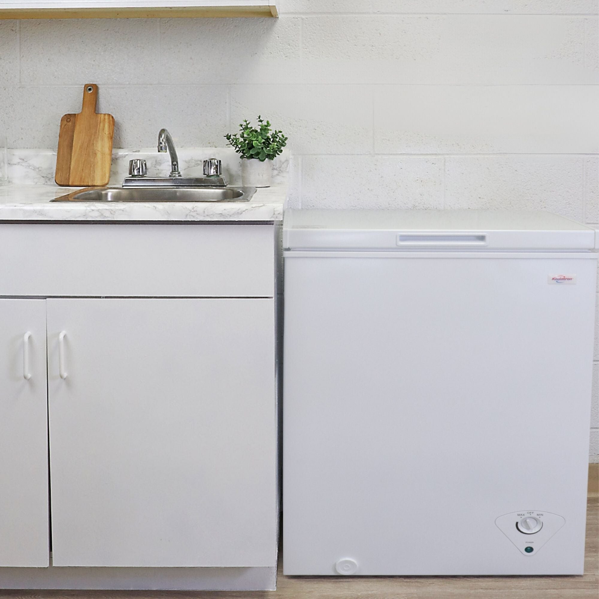 Koolatron white chest freezer, closed, beside a white kitchen cabinet with white marble countertop