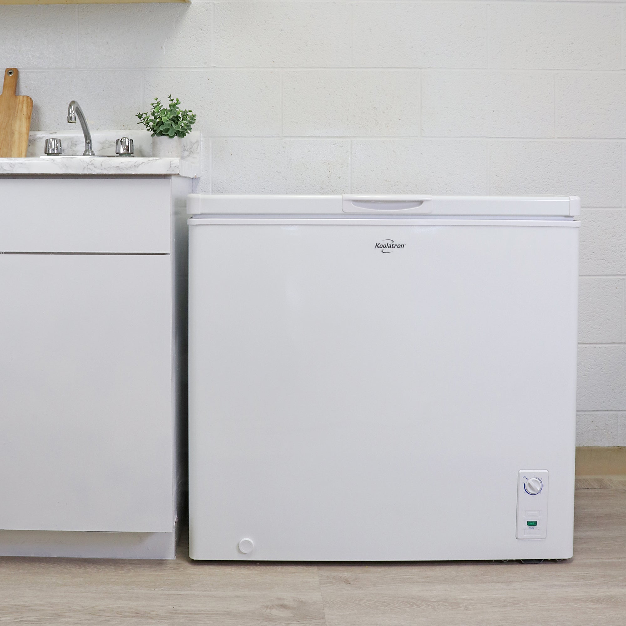 Koolatron white chest freezer, closed, beside a white kitchen cabinet with white marble countertop