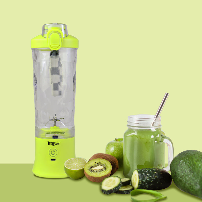 Lifestyle image of the Total Chef USB chargeable blender on a pale green background with an avocado, an apple, sliced cucumber, lime, and kiwi fruit, and a glass of green smoothie beside it.
