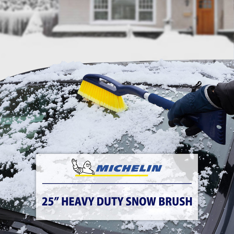 Lifestyle image of a gloved hand using the snow brush to remove snow from the windshield of a dark coloured car. Transparent white overlay at the bottom shows the MICHELIN logo above text reading "25" heavy duty snow brush"