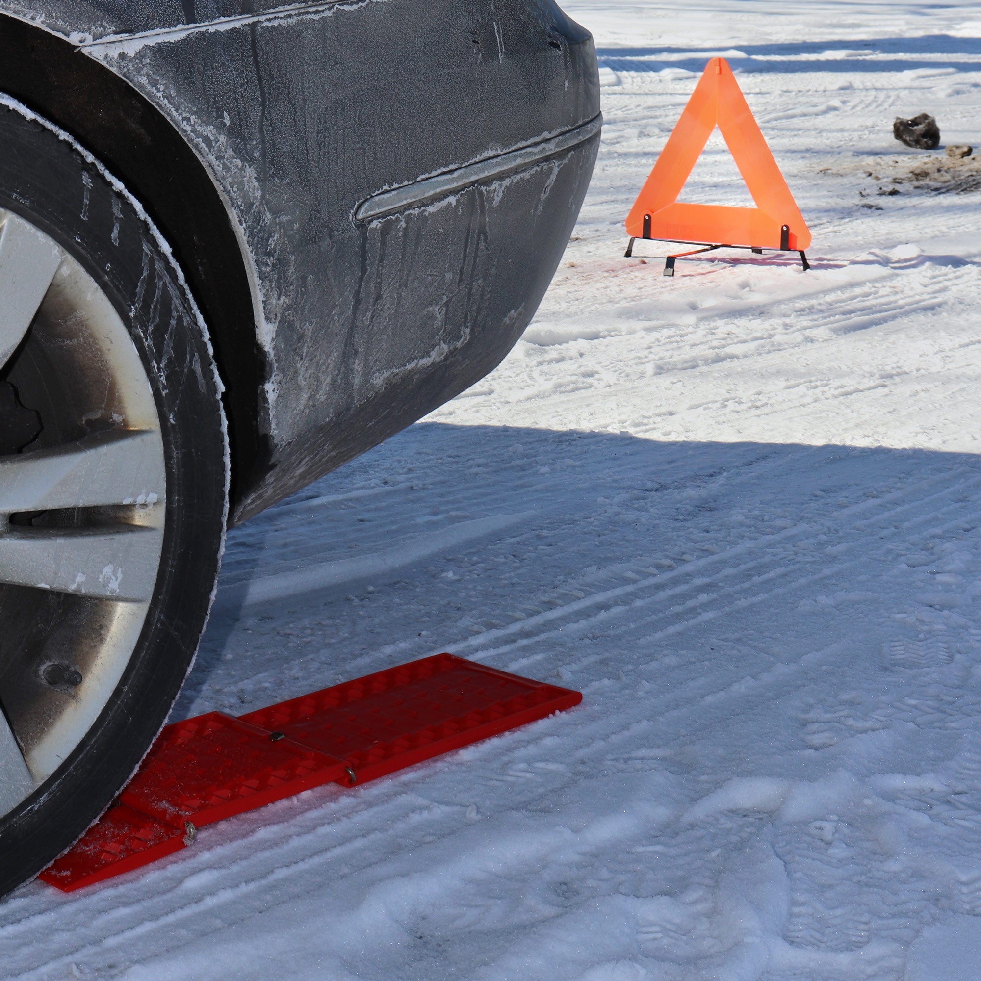 Lifestyle image shows a closeup view of the rear of a gray car on snow-covered ground with a traction strip under the tire and the warning triangle visible in the background