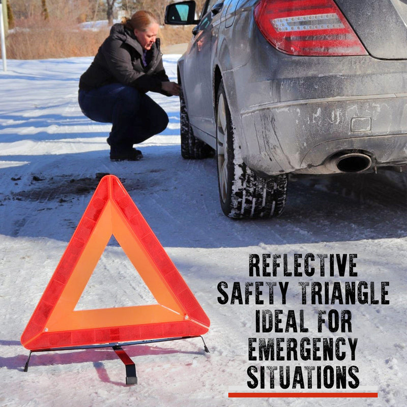Lifestyle image shows the reflective warning triangle set up on snow-covered ground in the foreground with a person with light skin, dark blonde hair tied back, and a dark winter coat, crouching beside the front wheel of a dark gray car in the background. Text overlay at the bottom right reads, "Reflective safety triangle ideal for emergency situations"