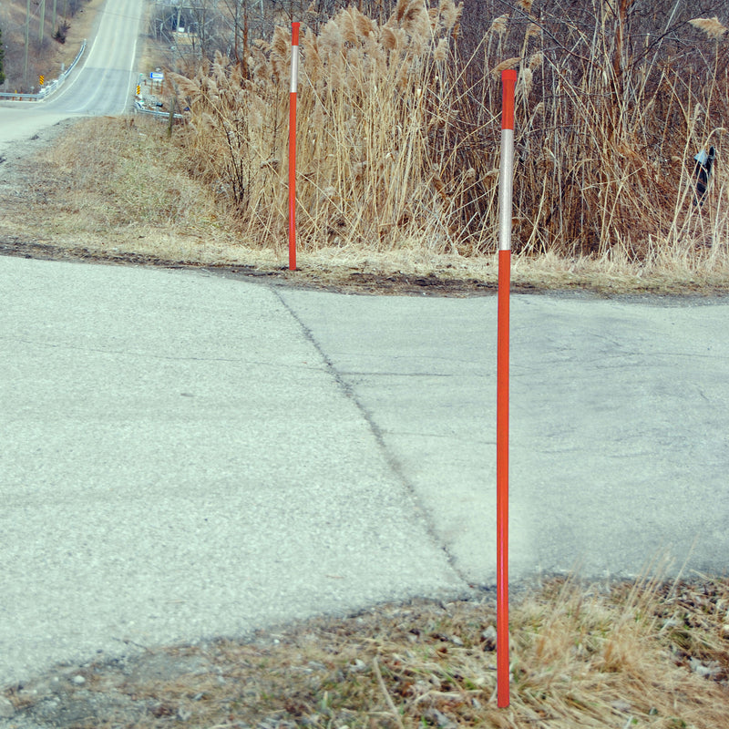 Lifestyle image of two orange driveway markers installed in the grass on either side of the entrance of a paved driveway coming off two-lane road