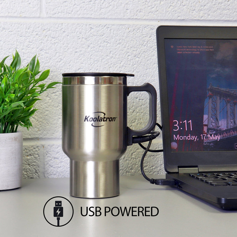 Lifestyle image of USB/12V travel mug with built-in heater plugged into the USB port of a black laptop on a white desk. There is a plant in a white pot to the left and text and icon below describe "USB powered"