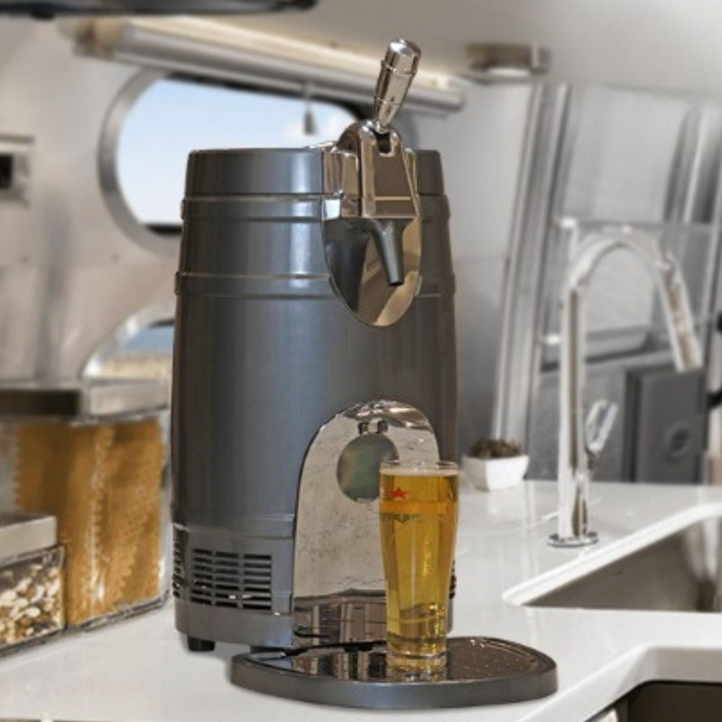 Lifestyle image of 5L beer keg cooler with a full glass positioned below the spout on a white counter inside a large boat with a stainless steel sink to the right and an oval porthole window behind.