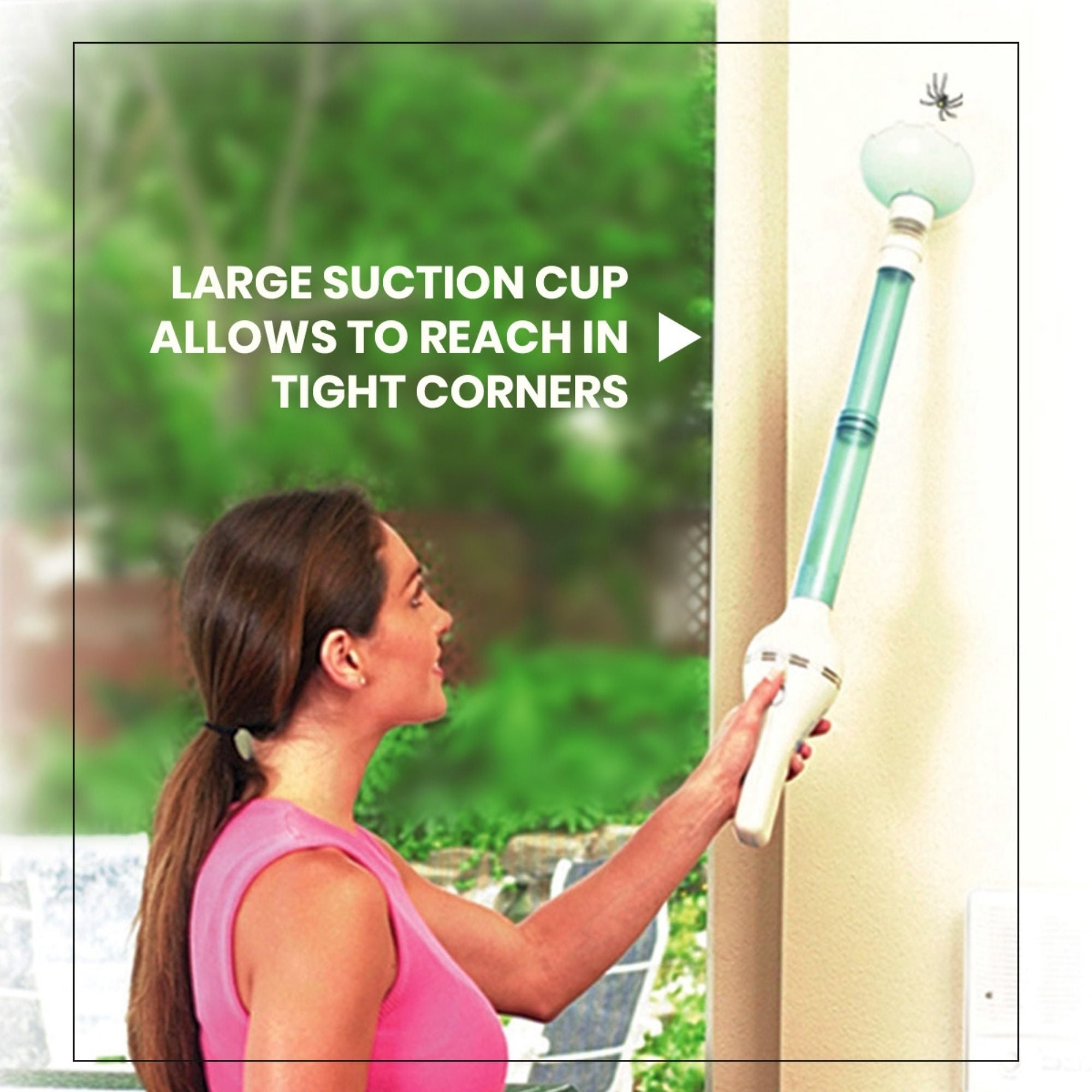 Lifestyle image of a person with light skin, long dark brown hair in a ponytail, and a pink sleeveless shirt using the bug vacuum to capture a spider high up on a beige wall beside a large exterior window showing a green space outdoors. Text overlay reads, "Large suction cup allows to reach into tight corners"