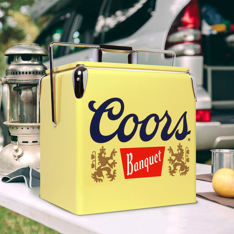 Lifestyle image of Coors Banquet retro ice chest with bottle opener on a white folding table with a metal lantern beside it and a vehicle in the background