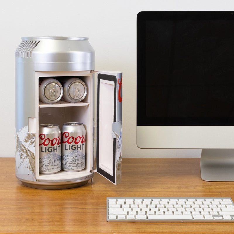 Lifestyle image of Coors Light can-shaped mini fridge, open with 6 cans of Coors Light beer inside, on a wooden desktop with a computer monitor and keyboard beside it