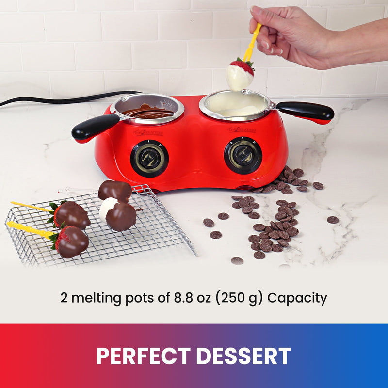 Lifestyle image of a hand dipping a strawberry in white melted chocolate in the chocolatiere on a white countertop. The other melting pot has milk chocolate in it and there is a cooling rack to the left with strawberries and marshmallows on it and unmelted chocolate discs scattered on the counter to the right. Text below reads "Perfect dessert: 2 melting pots of 8.8 oz (250 g) capacity"