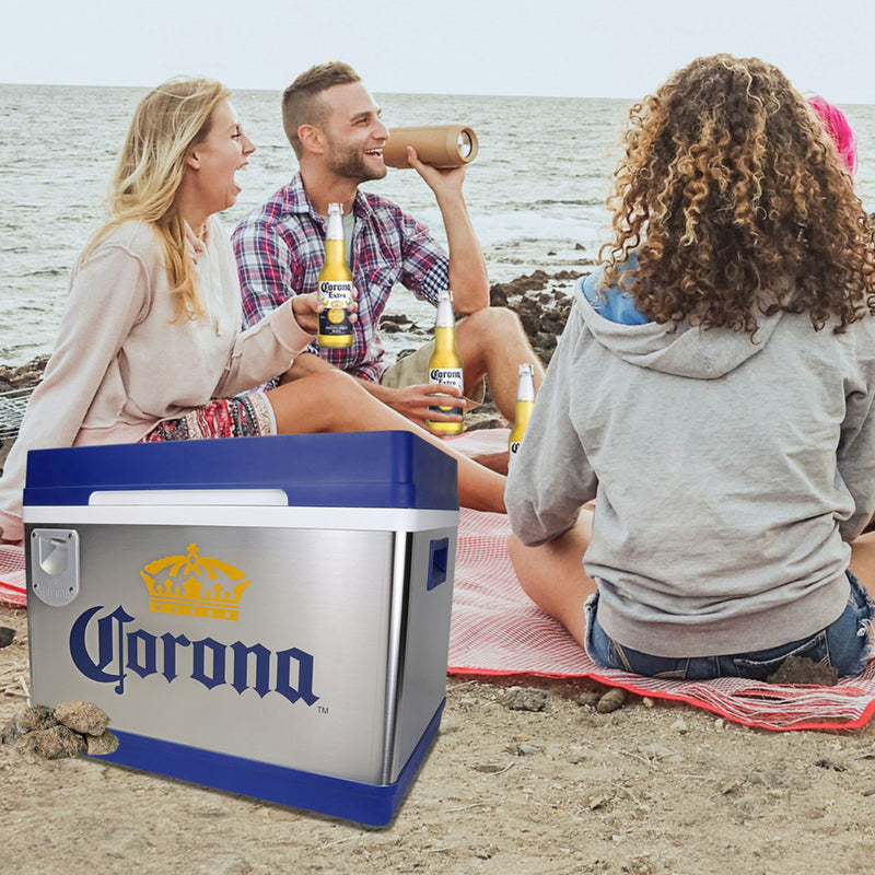 Lifestyle image shows a group of young adults sitting on a blanket on the beach holding bottles of Corona beer with the ocean in the background and a Corona Cruiser thermoelectric cooler beside them
