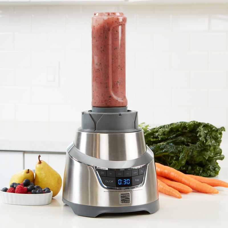 Lifestyle image of Elite 1.3 HP blender on white counter with a smoothie blended in the single-serving cup and fruits and vegetables beside
