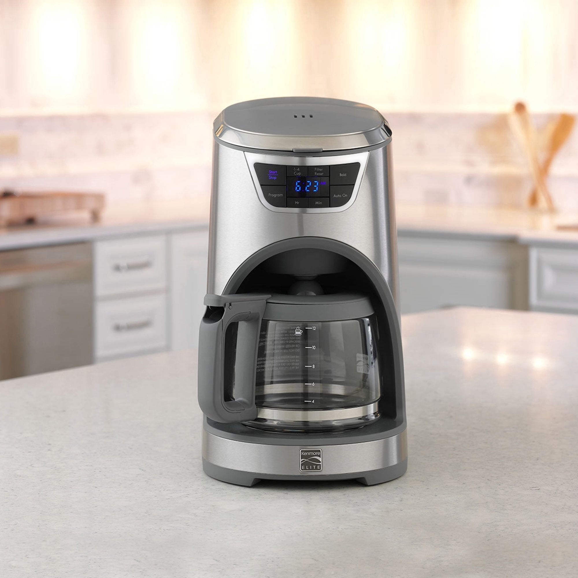 Lifestyle image of Kenmore Elite 12 cup programmable coffeemaker on a light gray countertop with white cupboards and drawers and stainless steel appliances in the background