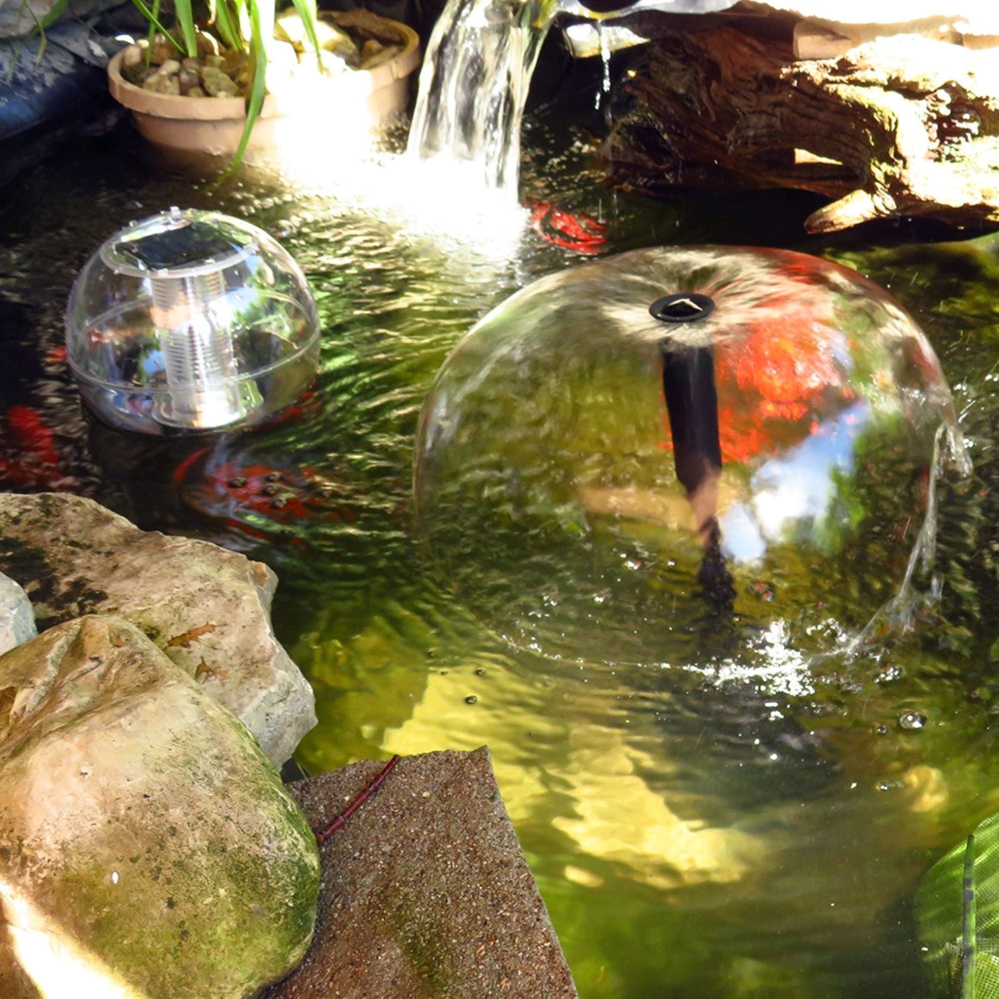 Lifestyle image of an in ground pond surrounded by plants and stones with a water bell fountain and floating solar lantern in the middle