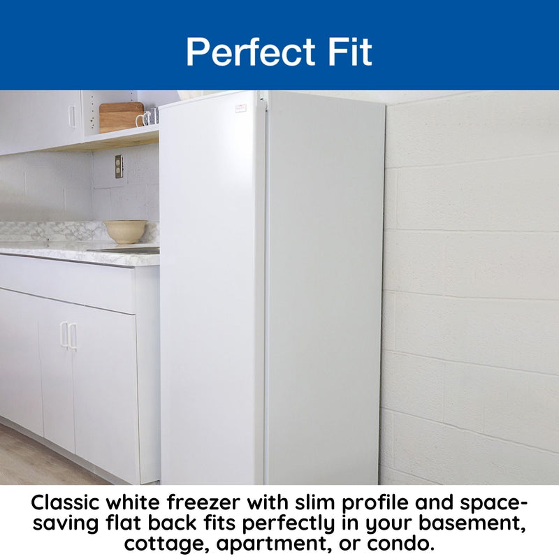 Lifestyle image of closed upright freezer on a light-colored wood floor beside a white kitchen cabinet with marble countertop. Text above reads, "Perfect fit," and text below reads, "Classic white freezer with slim profile and space-saving flat back fits perfectly in your basement, cottage, apartment, or condo"