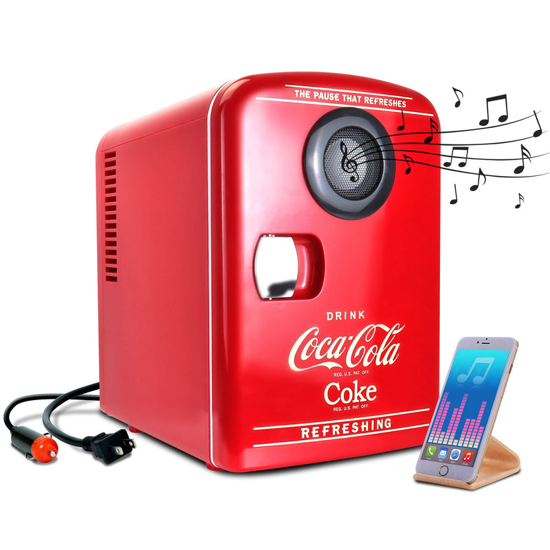 Product shot of Coca-Cola 4L mini fridge with Bluetooth speaker, closed, with AC and DC power cords visible, on a white background. There is a smartphone or music player on a stand in the foreground and small black music notes emanating from the speaker 