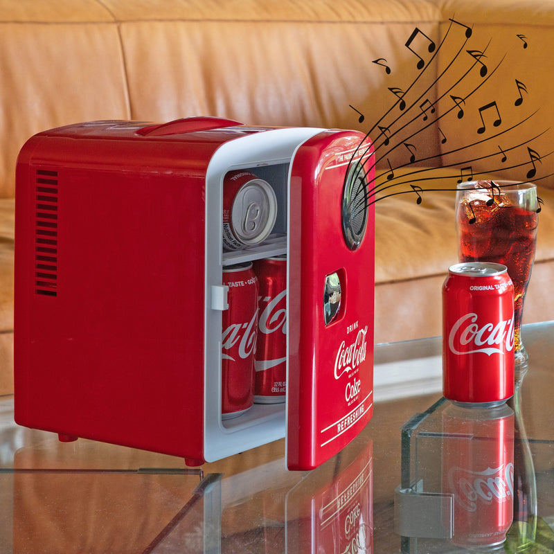 Lifestyle image of Coca-Cola 4L 12V cooler with Bluetooth speaker, partly open with cans inside, on a glass coffee table with a tan leather sofa behind it, a can and glass of Coke to the right, and small black music notes overlaid