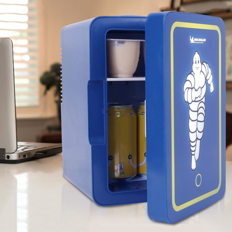 Lifestyle image of Michelin mini fridge, partly open with cans of pop and a yogurt cup visible, beside a laptop computer on a white desktop