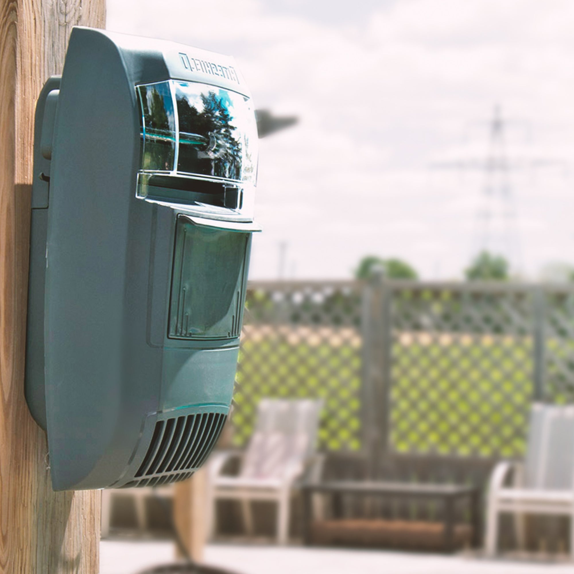 Lifestyle image of Bite Shield wall mount flying insect trap mounted on a wooden post outdoors with wooden deck and deck chairs in the background