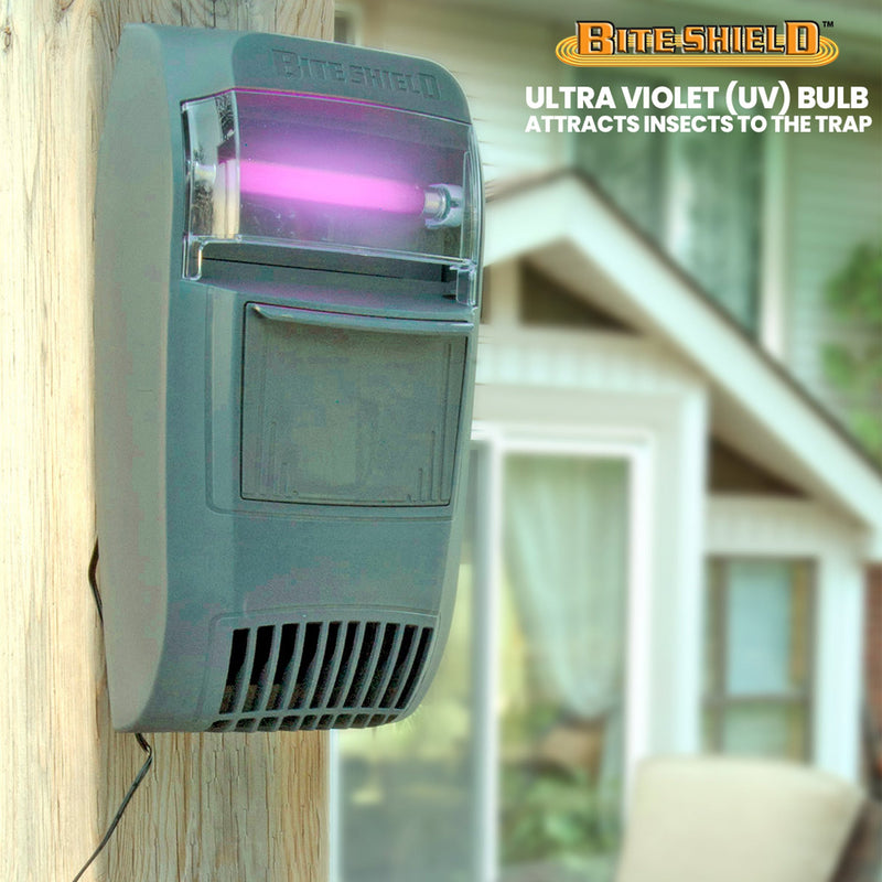 Lifestyle image of Bite Shield wall mount flying insect trap mounted on a wooden post outdoors with UV light illuminated and the exterior of a house in the background. Text above reads, "Bite Shield: Ultraviolet (UV) bulb attracts insects to the trap"