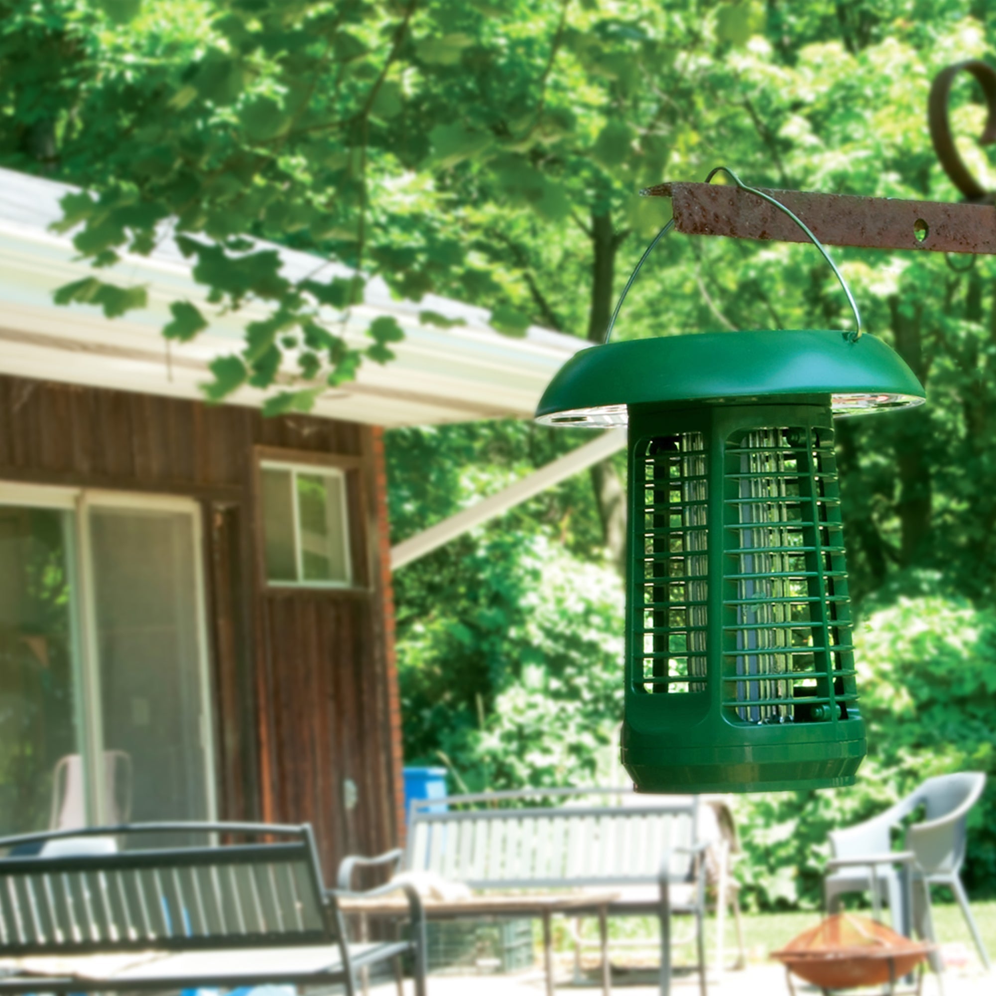 Lifestyle image of Bite Shield solar powered electronic flying insect zapper hanging from a tree branch outdoors with branches, leaves, and the exterior of a house in the background