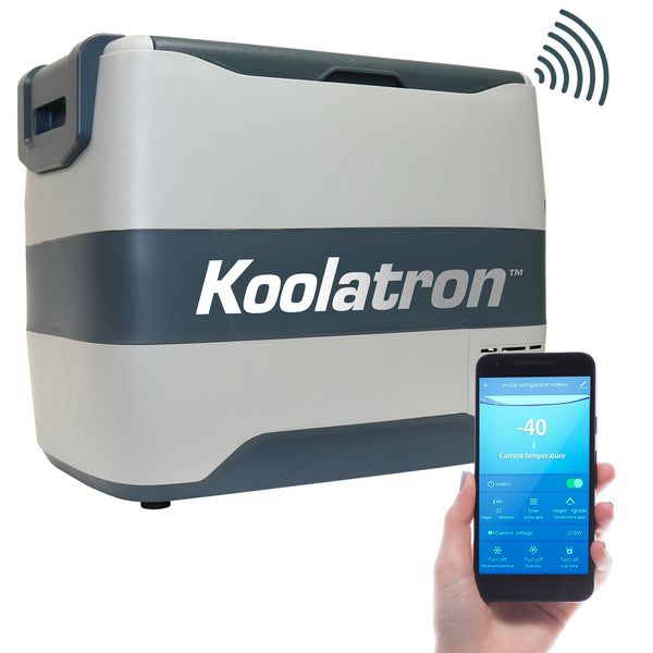 Product shot of 12V travel fridge/freezer on a white background with a person's hand holding a smartphone with the Koolatron Smart app on the screen in the foreground