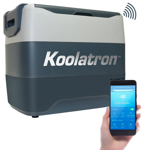 Product shot of 12V travel fridge/freezer on a white background with a person's hand holding a smartphone with the Koolatron Smart app on the screen in the foreground
